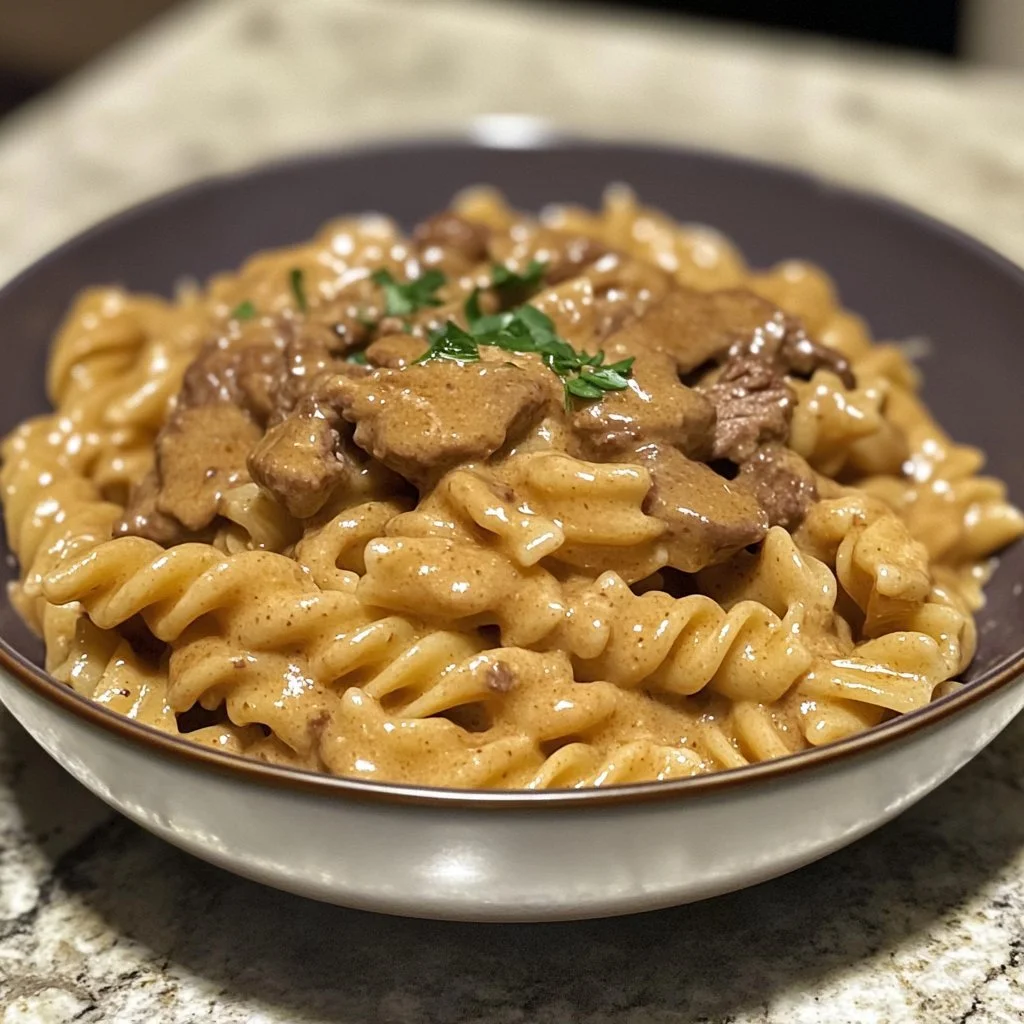 Creamy beef pasta dish served in a bowl with fresh herbs and grated cheese.